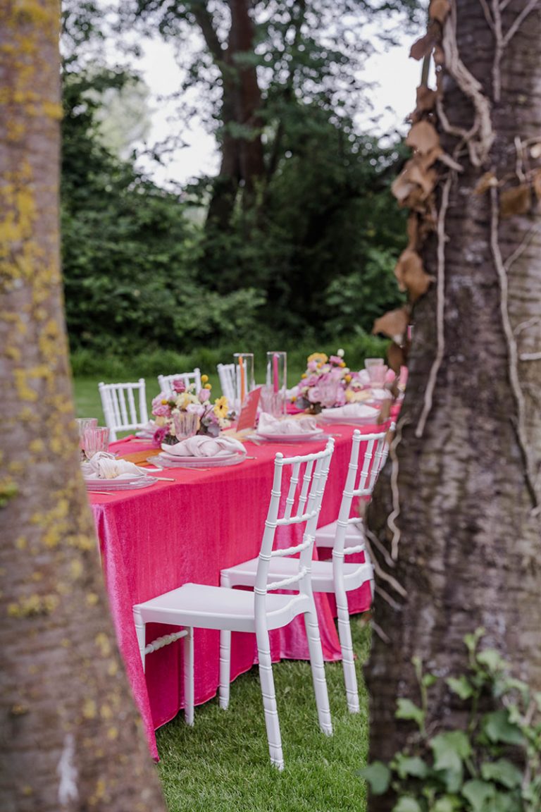 feierlich gedeckte Tische auf Rasen zwischen Baeumen im Freien