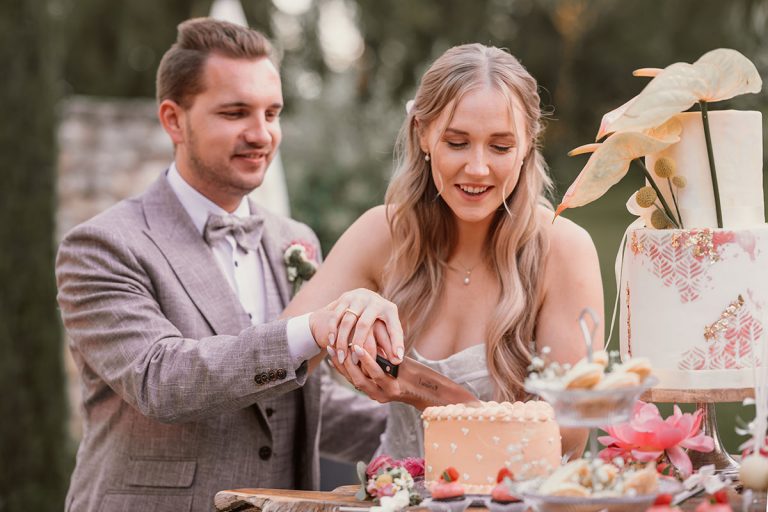 Brautpaar beim Anschneiden der Hochzeitstorte in zarten Pastelltönen